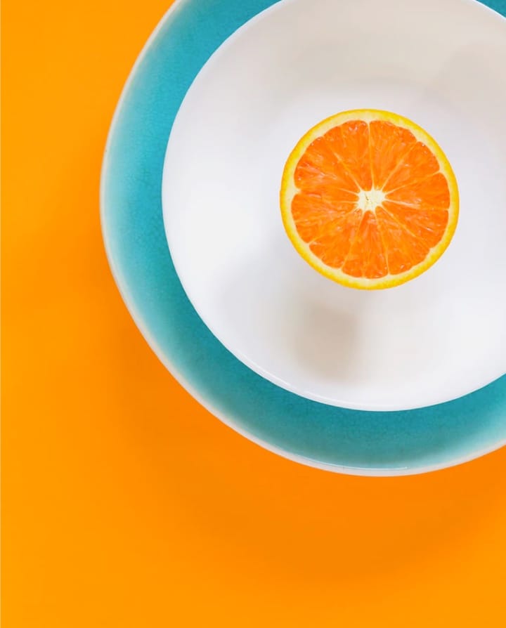 half an orange in a white bowl in a blue bowl with an orange coloured background